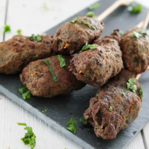 Skewers Of Grilled Lamb Kafta Served With Creamy Hoummos, Grilled Onions, And Tomato Slices.